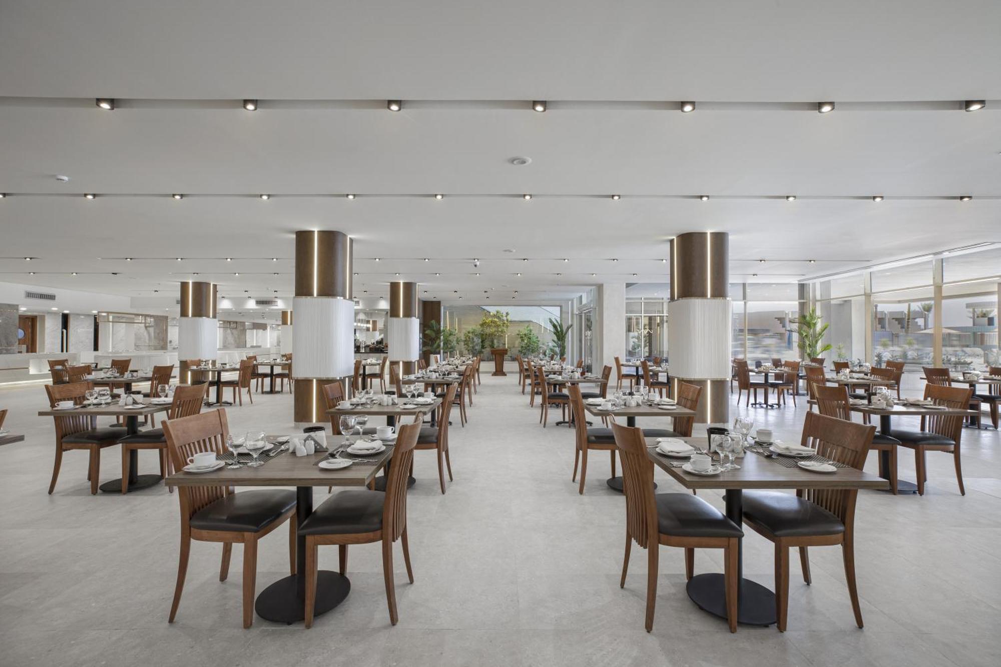 V Hotel Sharm El Shiekh Esterno foto The photo depicts a restaurant interior. The space features a modern design with several rows of wooden tables and chairs, neatly arranged for diners. Each table is set with dishes and cutlery, indicating readiness for service. Bright lighting is pro