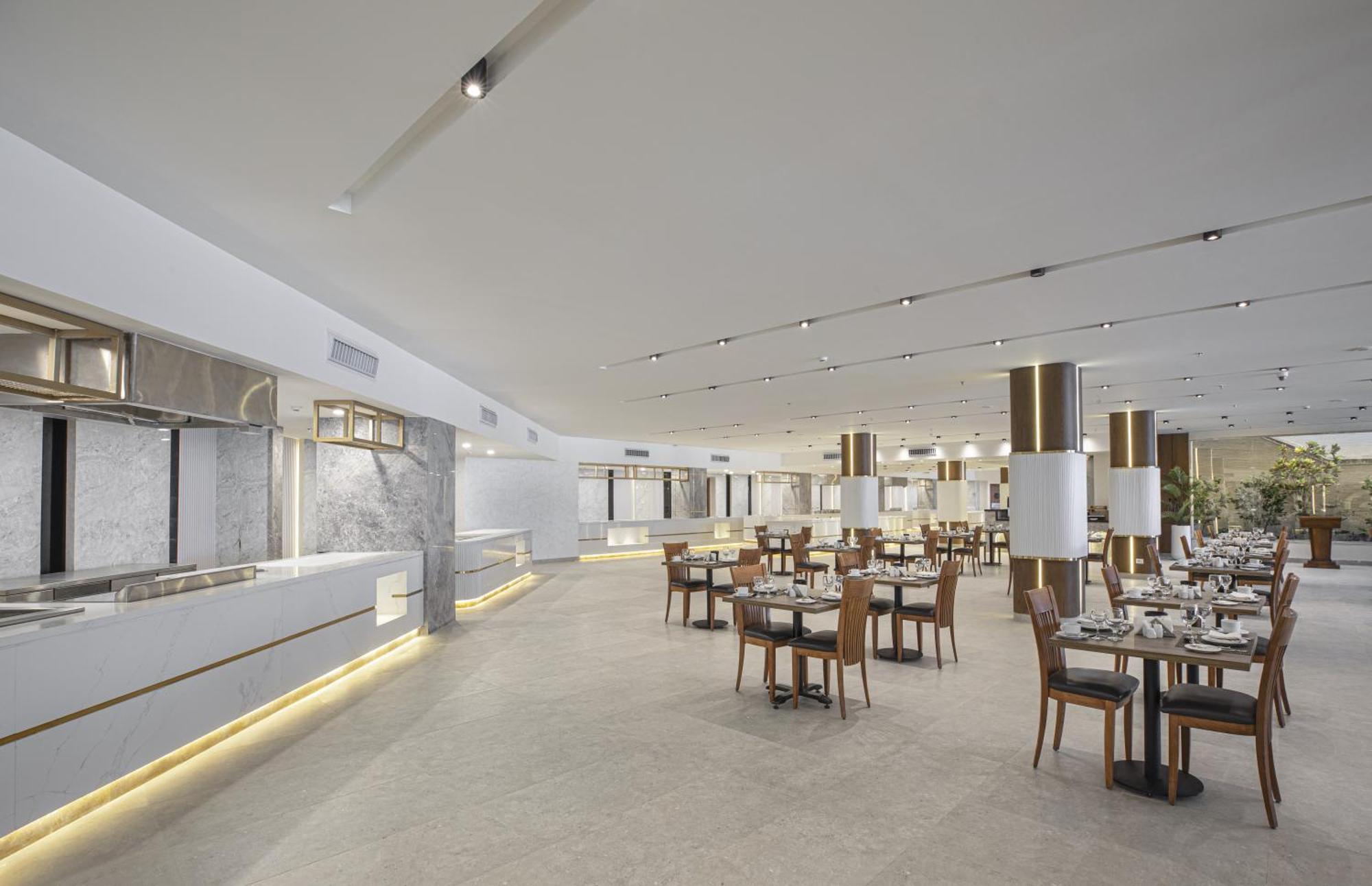 V Hotel Sharm El Shiekh Esterno foto The photo depicts a modern restaurant interior. The space features a bright and airy ambiance with large windows and an open layout. There are several tables arranged neatly across the floor, surrounded by wooden chairs. The decor includes light-colo