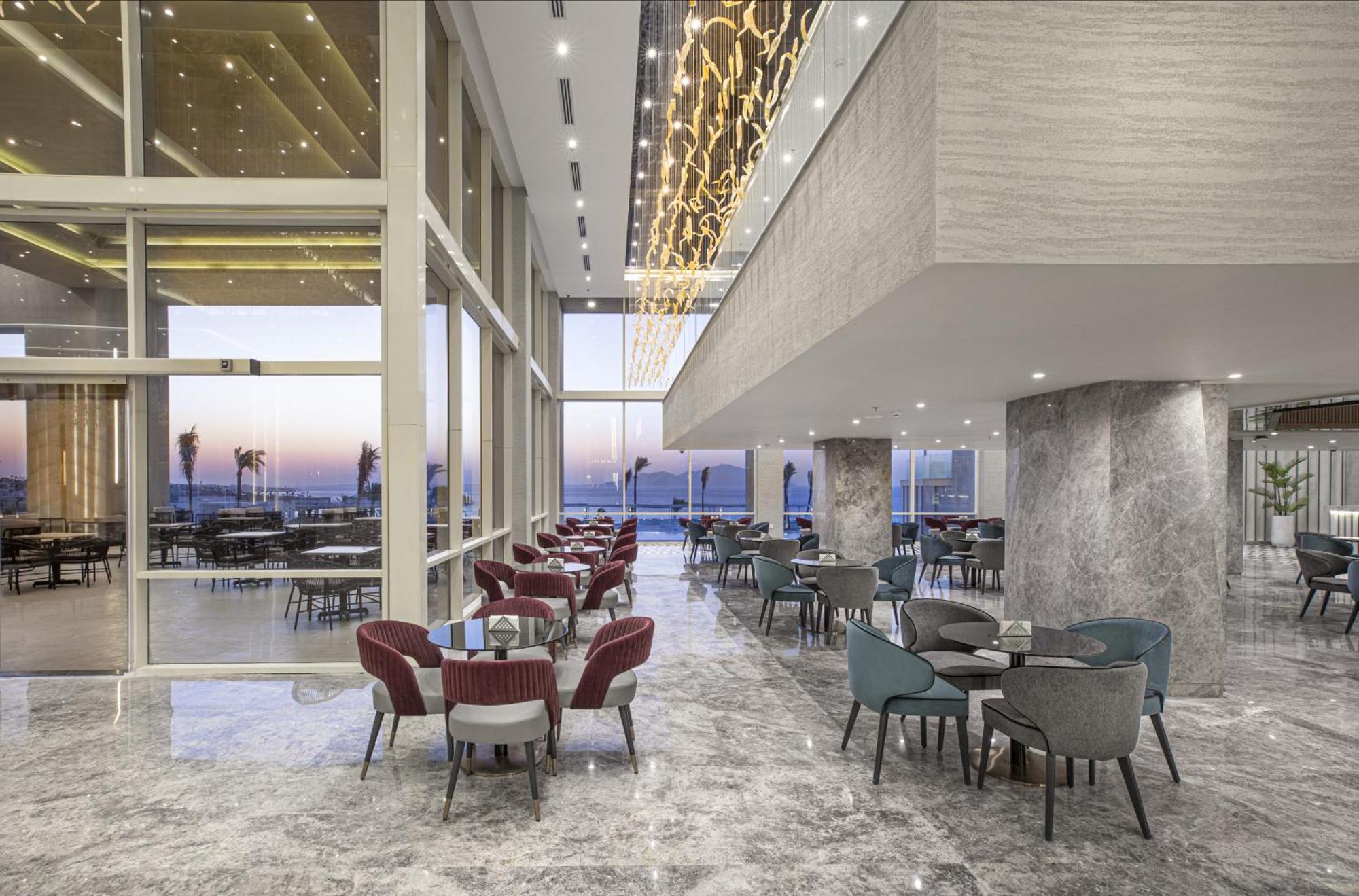 V Hotel Sharm El Shiekh Esterno foto The photo showcases a modern dining space or lounge area featuring large windows that provide a view of the outdoors, likely overlooking a scenic landscape or waterfront. The interior design includes elegant marble flooring and stylish furniture, com