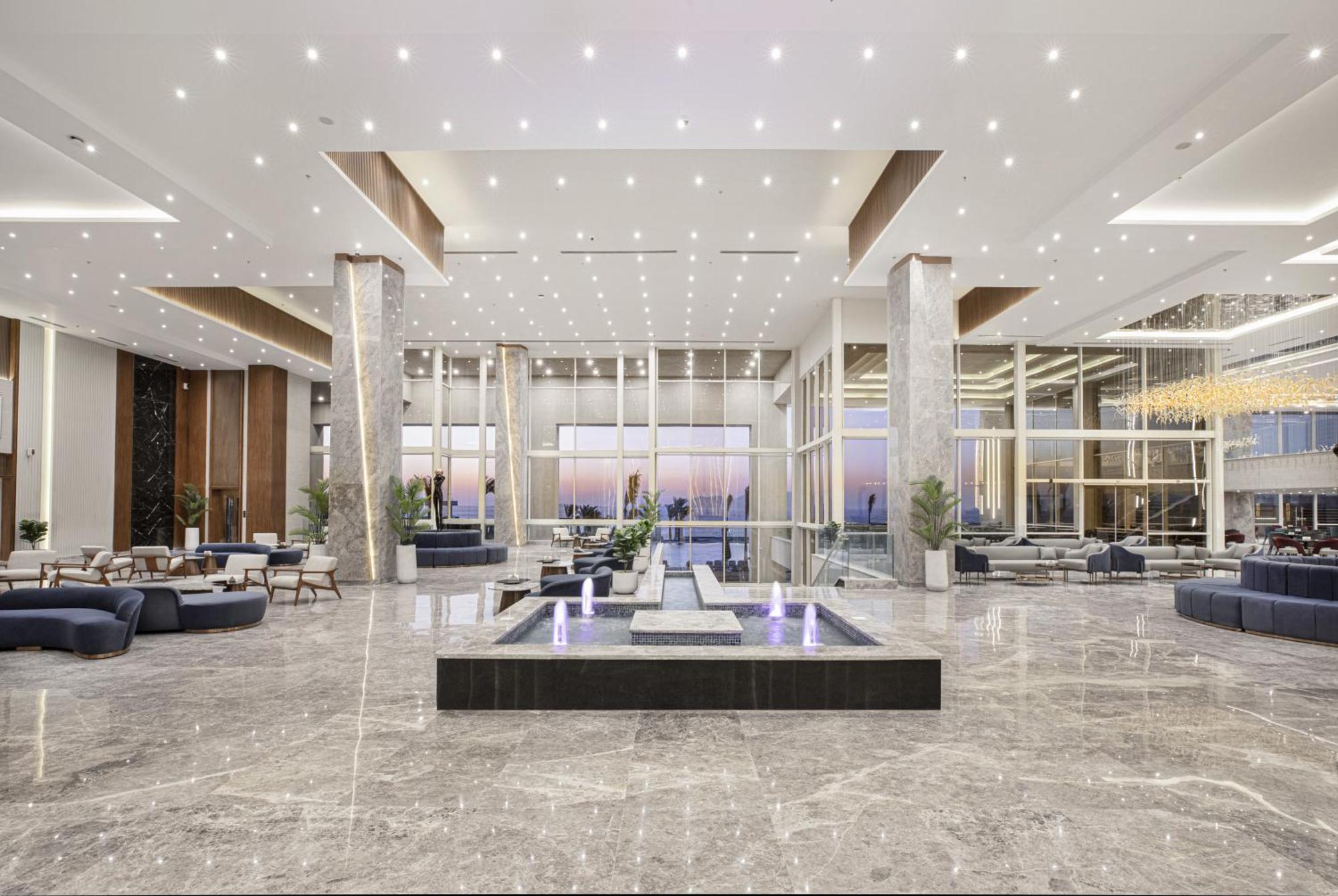 V Hotel Sharm El Shiekh Esterno foto The photo shows a modern and spacious lobby area. It features high ceilings with numerous recessed lights creating a bright atmosphere. The flooring is made of glossy marble, adding to the elegance of the space. 

In the center, there is a sleek wate
