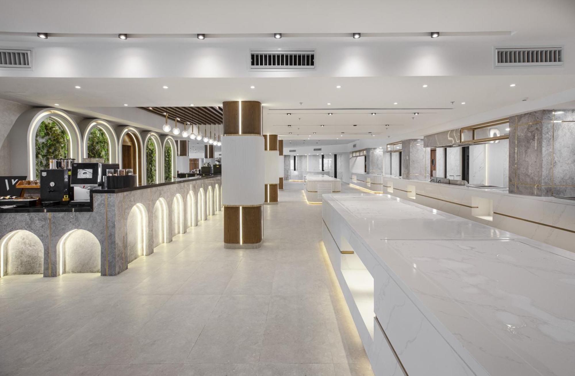 V Hotel Sharm El Shiekh Esterno foto The photo shows a modern, spacious interior, likely of a commercial space such as a café or a restaurant. The design features a light color palette, with white walls and smooth surfaces. There are elegant arch-shaped windows along one side, adding a 