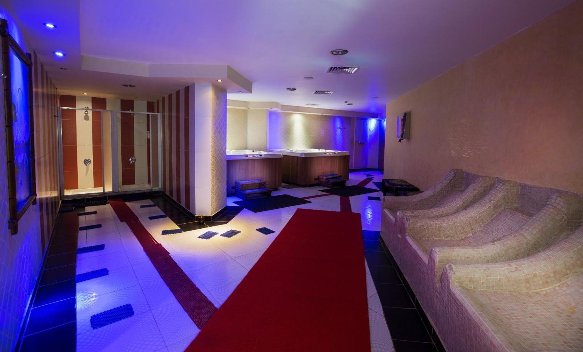 V Hotel Sharm El Shiekh Esterno foto The photo shows a modern interior space, likely a luxurious spa or relaxation area. It features a well-lit corridor with soft blue lighting. There is a red carpet leading down the center, bordered by black and white tile patterns. On one side, there 