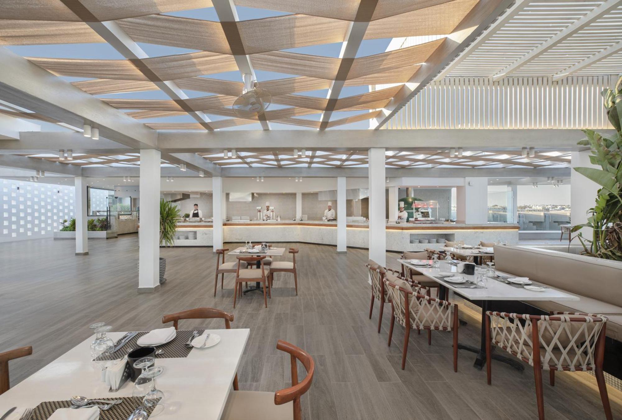 V Hotel Sharm El Shiekh Esterno foto The photo shows a modern and spacious restaurant interior. The design features a light and airy atmosphere with large windows allowing for natural light. There are wooden beams in the ceiling, and the floor is made of light-colored wood, contributing