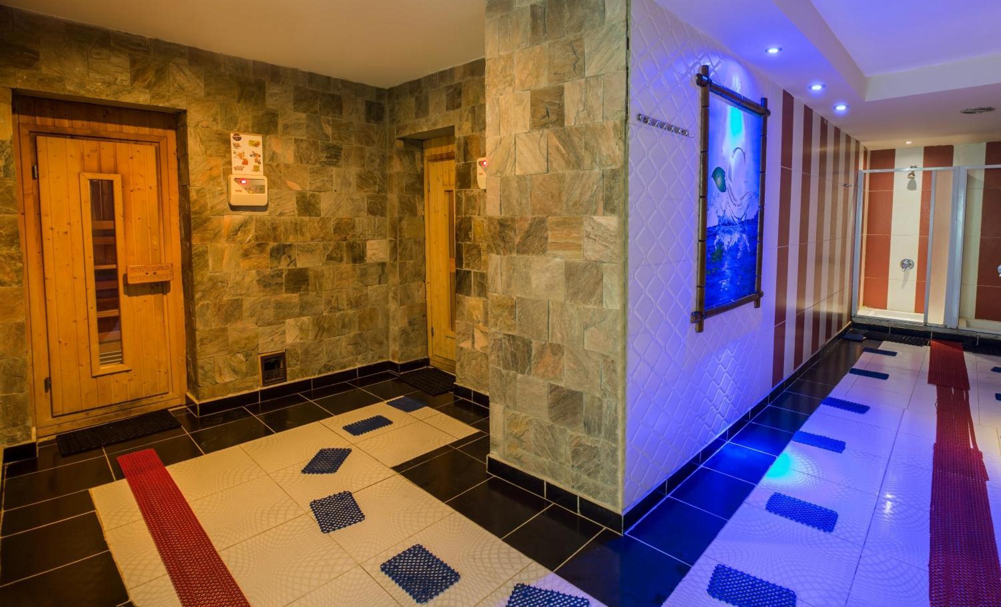 V Hotel Sharm El Shiekh Esterno foto The photo shows an interior space that appears to be a spa or wellness area. The walls are made of natural stone, giving a serene and earthy feel. There are wooden doors on one side, likely leading to sauna or treatment rooms. The floor has a unique 